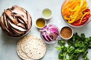 ingredients laid out for vegan fajitas, portobello mushrooms, bell peppers, onions, cilantro and tortillas