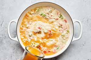 vegetable stock being added to a skillet with milk, butter, carrots, celery, onion, flour and spices