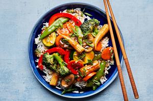 vegetable stir fry made with mushrooms, broccoli, corn, pepper, snap peas, zucchini & carrots on top of rice with chopsticks