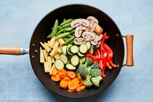 mushrooms, broccoli, corn, pepper, snap peas, zucchini & carrots being cooked in vegetable oil in a wok