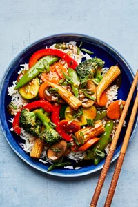 vegetable stir fry made with mushrooms, broccoli, corn, pepper, snap peas, zucchini & carrots on top of rice with chopsticks