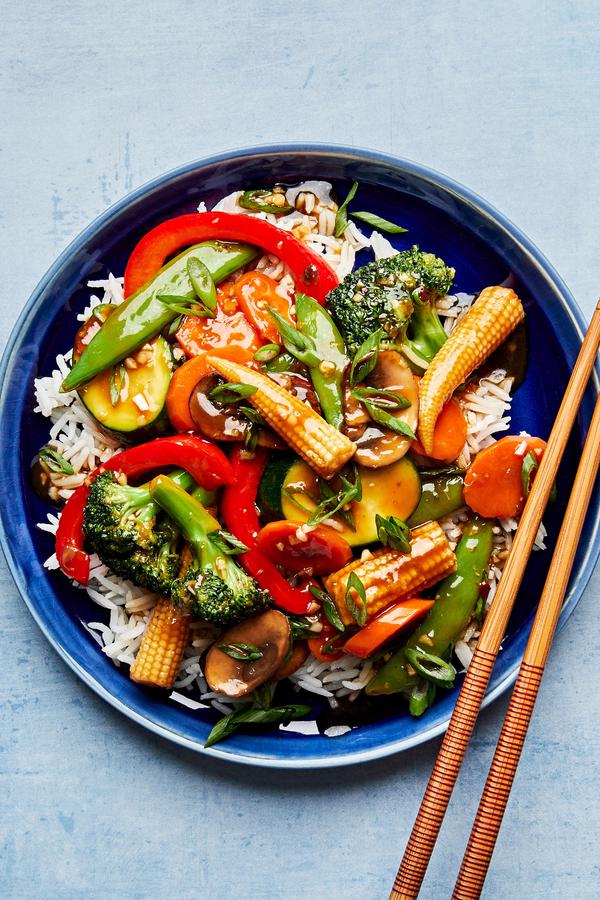 vegetable stir fry made with mushrooms, broccoli, corn, pepper, snap peas, zucchini & carrots on top of rice with chopsticks