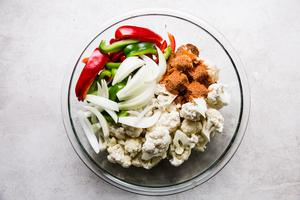cauliflower, red and green bell peppers, onion and taco seasoning in a glass mixing bowl