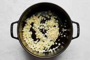 garlic and onion being cooked in olive oil in a large soup pot