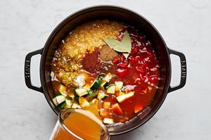 vegetable stock, creamed corn, tomatoes, enchilada sauce, zucchini, chilies and spices being added to  a soup pot