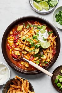 a bowl of vegetarian tortilla soup topped with cheese, sour cream, cilantro, avocado and lime wedges