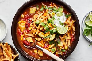 a bowl of vegetarian tortilla soup topped with cheese, sour cream, cilantro, avocado and lime wedges