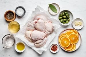 chicken thighs, salt, olive oil, oranges, vinegar, olives, bay leaf, cloves, red pepper flakes and pepper in bowls