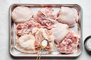 raw chicken thighs being seasoned salt on a sheet pan