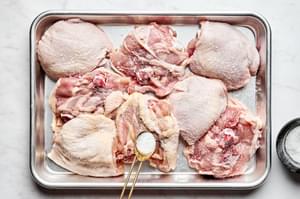 raw chicken thighs being seasoned salt on a sheet pan