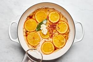 vinegar, olive brine and spices added to a pan with orange slices