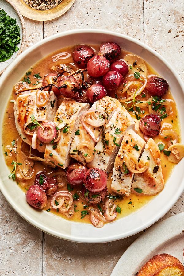 oven baked chicken breast sliced in a serving bowl with cooked shallots, parsley and red grapes