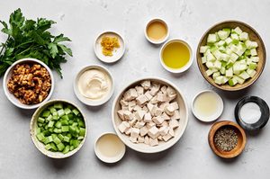 ingredients laid out to make homemade waldorf salad with creamy dressing including chicken, candied walnuts, grapes & apples