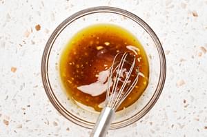 white balsamic vinegar, minced garlic, brown sugar, olive oil, salt, and pepper being whisked together in a bowl