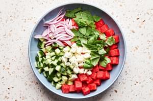 watermelon, cucumber, onions, feta, mint and basil in a bowl