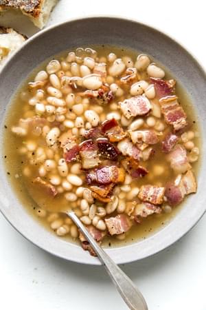 white bean and bacon soup in a bowl with a spoon