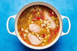 white bean chicken chili cooing in a pot made with onion, green enchilada sauce, chiles, spices, corn and bell pepper