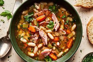 a bowl of white bean and ham soup made with olive oil, onion, carrots, celery, garlic & spices topped with pepper & parsley
