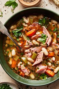 a bowl of white bean and ham soup made with olive oil, onion, carrots, celery, garlic & spices topped with pepper & parsley