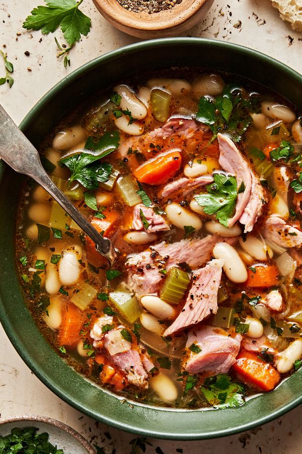 a bowl of white bean and ham soup made with olive oil, onion, carrots, celery, garlic & spices topped with pepper & parsley