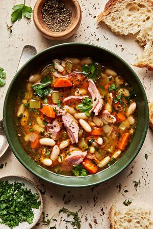 a bowl of white bean and ham soup made with olive oil, onion, carrots, celery, garlic & spices topped with pepper & parsley