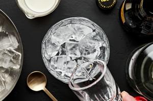 vodka being poured over ice in a cocktail glass