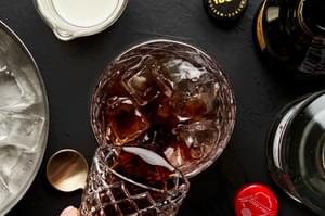 coffee liqueur being poured into a cocktail glass with vodka and ice