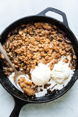 Caramel apple crisp with oats and vanilla ice cream in a cast iron skillet