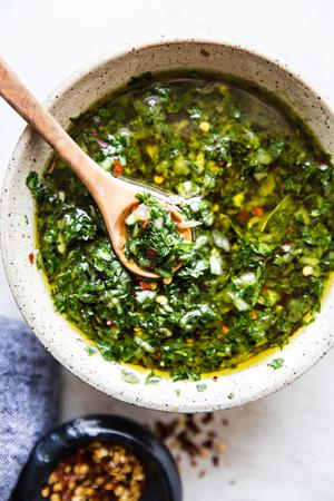 chimichurri sauce made with shallot, herbs , salt, pepper, olive oil, red wine vinegar next to a bowl of red pepper flakes
