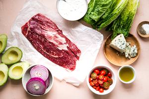 ingredients laid out for steak salad flank steak, romaine lettuce, onions, tomatoes blue cheese and avocados