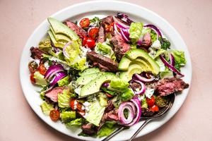 grilled steak salad with avocados, onions, tomatoes and a homemade blue cheese dressing on a large plate