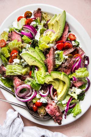 grilled steak salad with avocados, onions, tomatoes and a homemade blue cheese dressing on a large plate