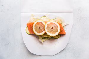 zucchini, fennel and salmon with dill, salt and pepper with lemon slices on parchment paper for en papillote