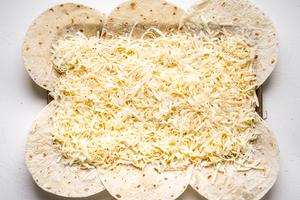flour quesadillas on a baking sheet with shredded cheese