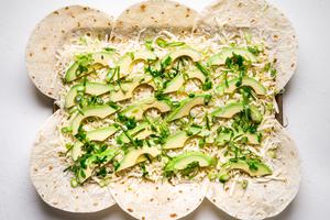 flour tortillas on a baking sheet with shredded cheese, avocado and green onions.