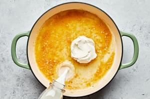 olive oil, garlic, butter, chicken stock, milk, and cream cheese being cooked in a skillet
