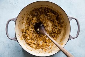 onion and garlic being cooked in a soup pot.